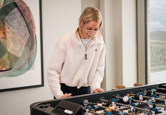 A woman in a white sweatshirt is playing a foosball table.
