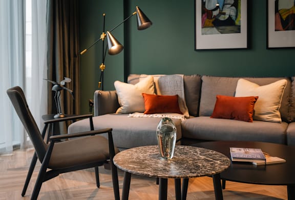 A living room with a grey sofa, a black chair, and a round table with a vase on it.