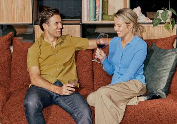 A man and a woman are sitting on a red couch, each holding a glass of wine.