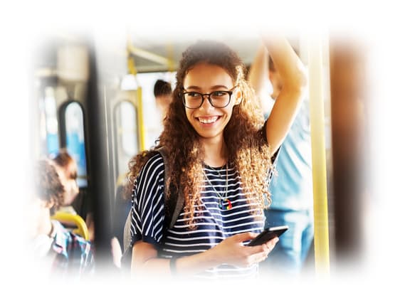a young woman with curly hair and glasses is holding her phone and smiling