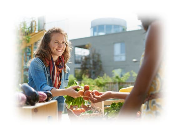 a woman sells vegetables at a farmers market on a sunny day