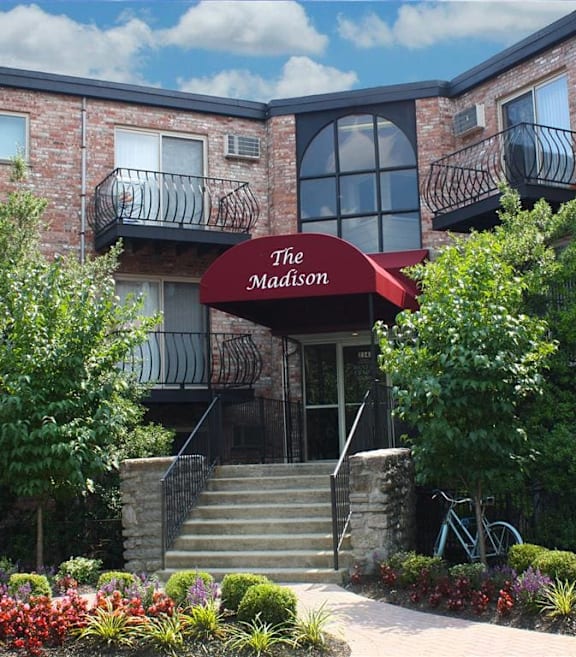 The front of a building called The Madison with a red awning and a bicycle leaning against a tree.