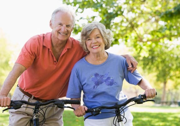 an older man and woman standing with their bikes