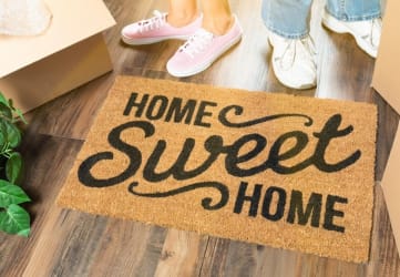 a home sweet home welcome mat on the floor with a family of four standing next to it