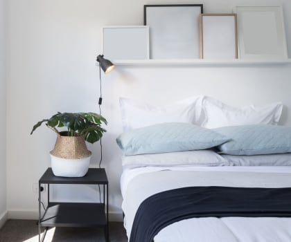 a bedroom with white walls and a white bed with blue bedding and a black nightstand