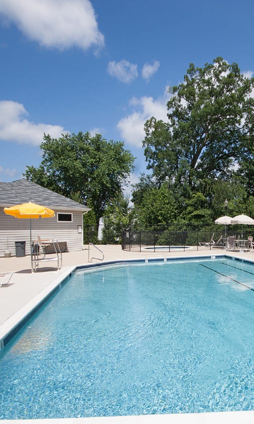 a swimming pool with chairs and umbrellas in front of a house at The Summit at Owings Mills Apartments, Owings Mills Maryland