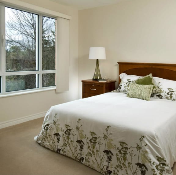 A bedroom with a large window and a bed with a white comforter