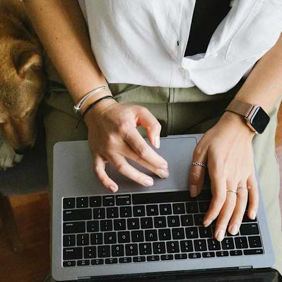 a woman typing on a laptop computer next to a dog