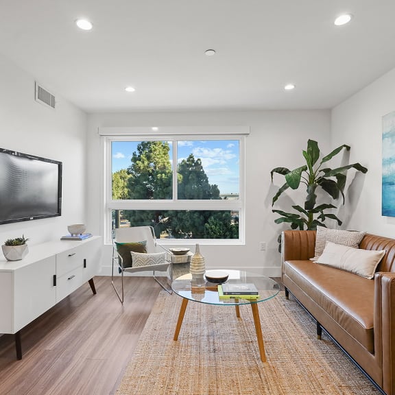 a living room with white walls, a large window, a leather couch and a glass coffee