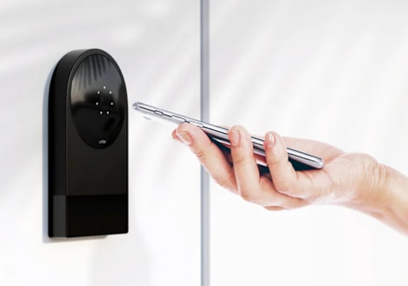 A hand holding a phone is touching a wall-mounted device.