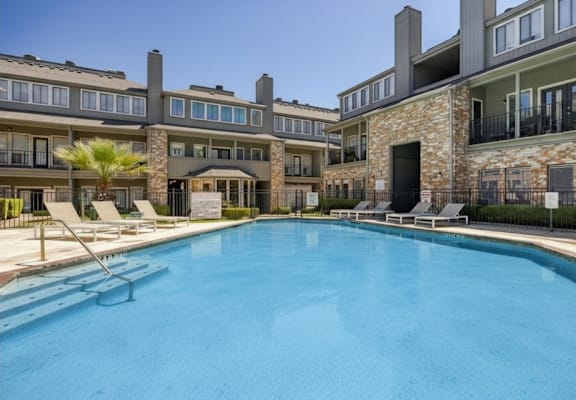 A large swimming pool in front of a building with lounge chairs around it.