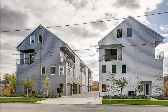 Two modern houses with balconies and large windows are situated on a street.