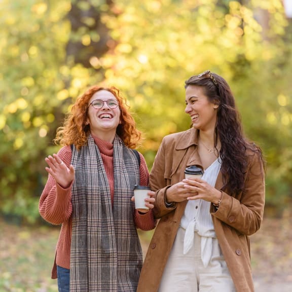 two women talking and laughing while holding coffee cups