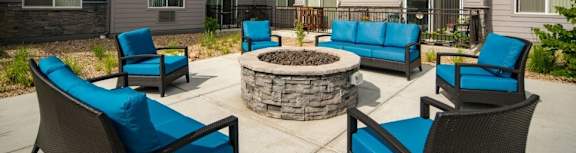 A patio with blue cushioned chairs and a fire pit.