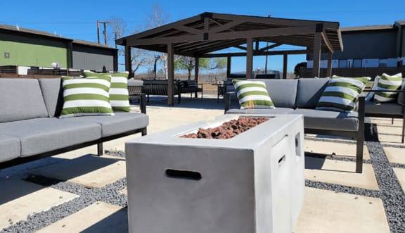 a concrete fire pit with pillows and couches in front of a pavilion at Ivy Plains at Brooks Apartments, San Antonio