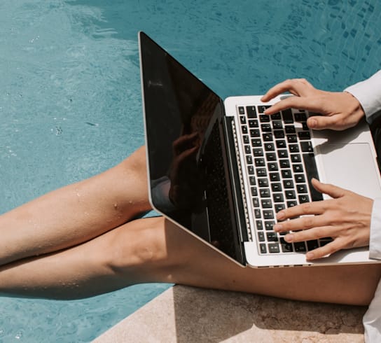 A person is using a laptop by the poolside.