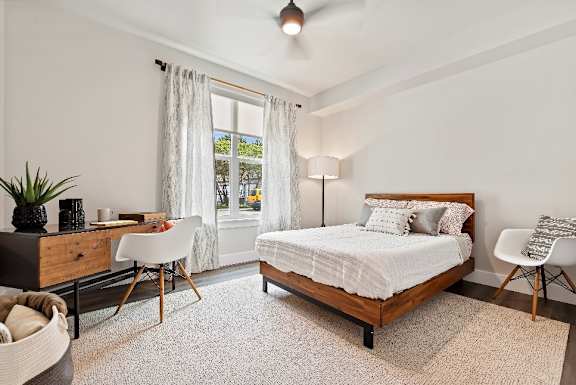A bedroom with a large bed, a desk with a chair, and a window with curtains.