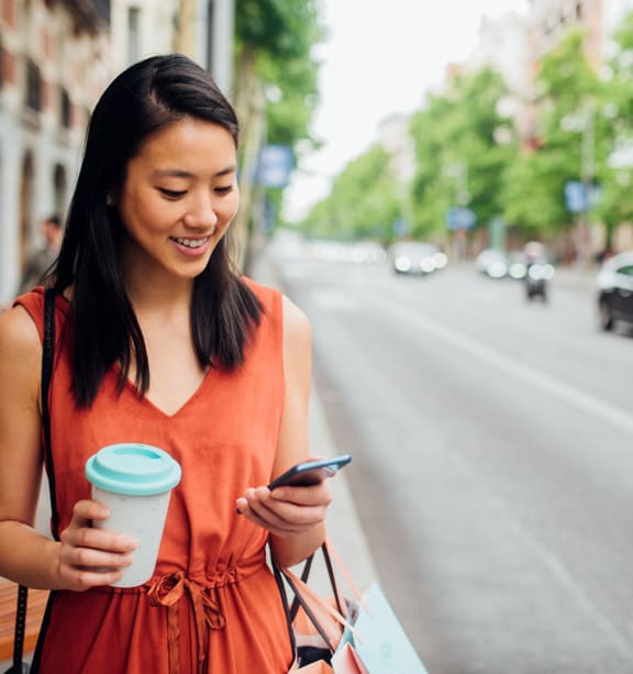 a woman walking down the street looking at her phone and holding a cup of coffee