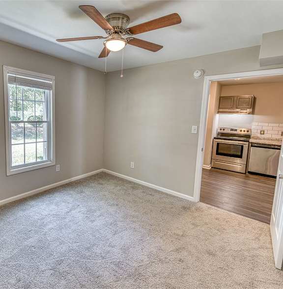 an empty living room with a ceiling fan and a kitchen