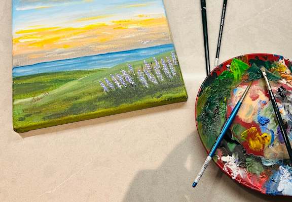A painting of a sunset over a field with a palette and paintbrushes.