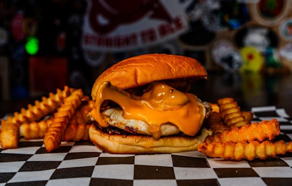 A burger with cheese and fries on a checkered table.