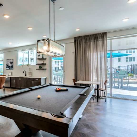 A pool table is in the middle of a room with a bar and a dining table.