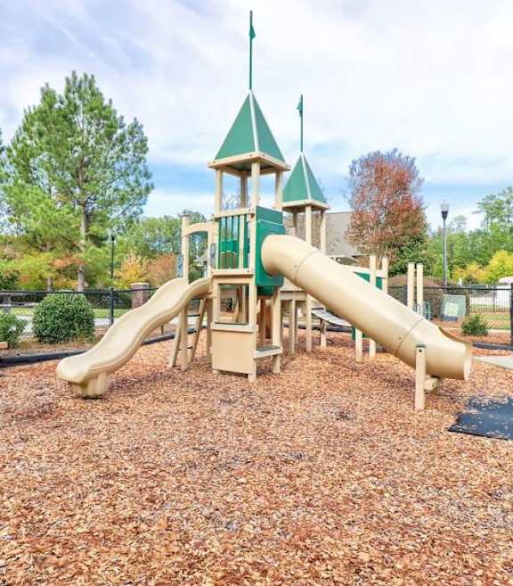 A playground with a green and yellow slide and a wooden structure.