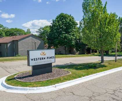 A sign for Western Pines Apartments stands in front of a building and trees.