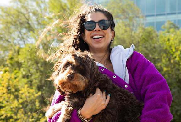 A woman in a purple jacket holding a brown dog.
