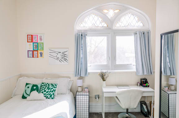 A white bedroom with a bed, desk, and window.