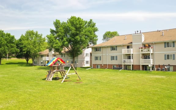 a playground sits in the middle of a grassy area in front of an apartment complex