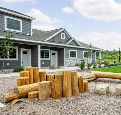 an outdoor play area with logs and rocks in front of a gray house