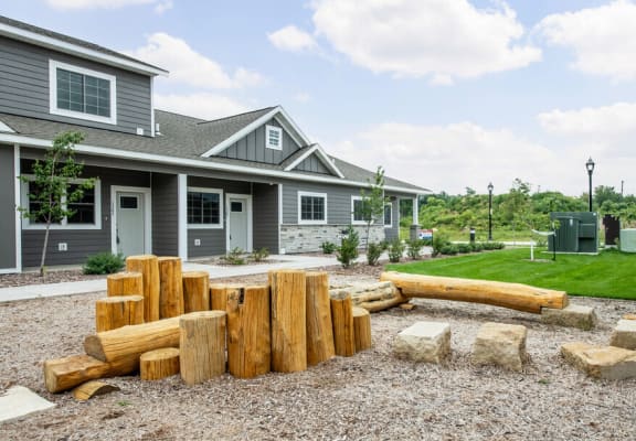 an outdoor play area with logs and rocks in front of a gray house