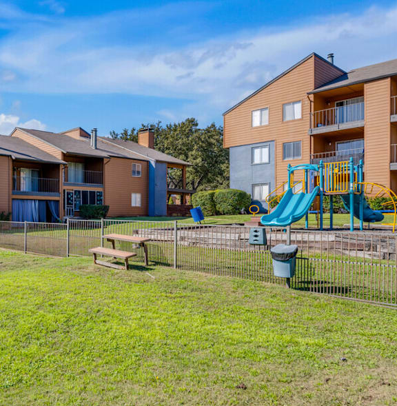 A playground with a slide and a fire hydrant is in front of apartment buildings.