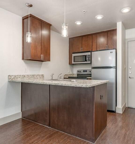 A kitchen with brown cabinets and a marble countertop. at Hickory Street Lofts Apartments, Denton, TX, 76201