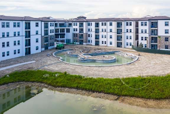 A large white building with a pool in the middle of a grassy area.