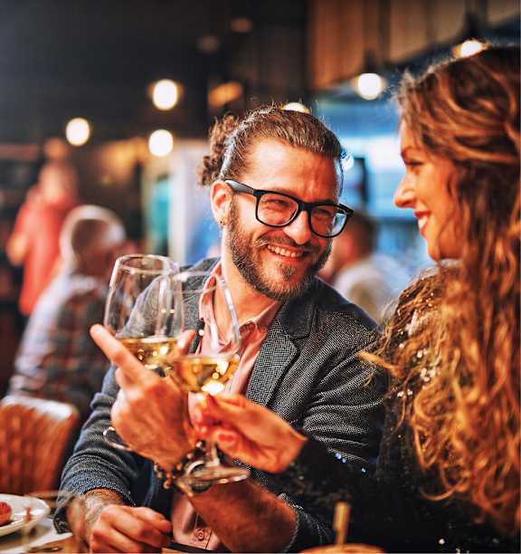 A man and a woman are toasting with wine glasses in a dimly lit restaurant.