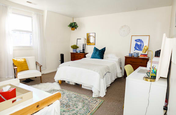 A white bedroom with a bed, nightstand, and chair.