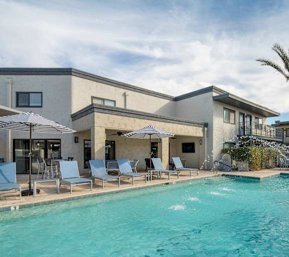A swimming pool in front of a building with palm trees.