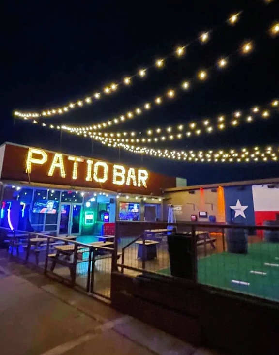 A bar named Patio Bar is lit up at night.