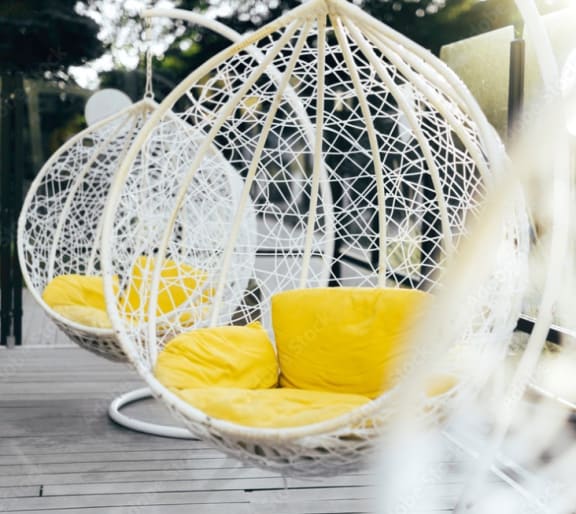 two white hanging chairs with yellow pillows on a wooden table