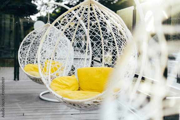 two white hanging chairs with yellow pillows on a wooden table
