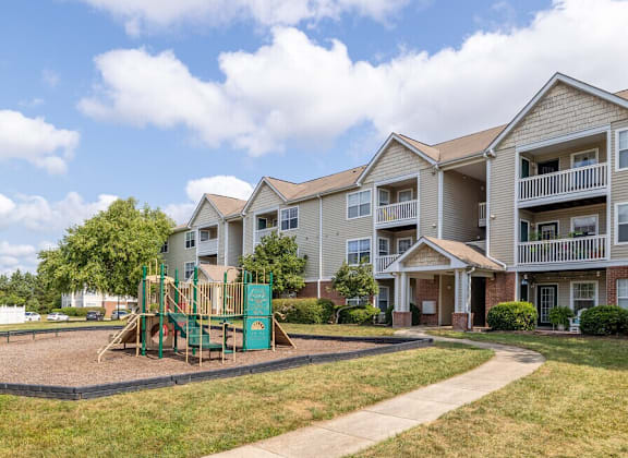 A playground with a green slide is in front of apartment buildings.
