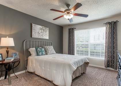 A bedroom with a bed, a ceiling fan, and a window with curtains.