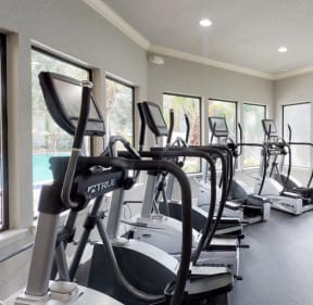 a gym with cardio equipment and a pool in the background