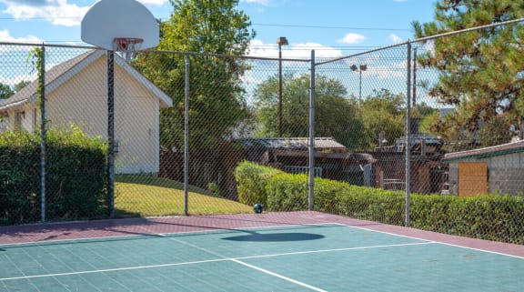 a tennis court in a fenced in area with a basketball hoop