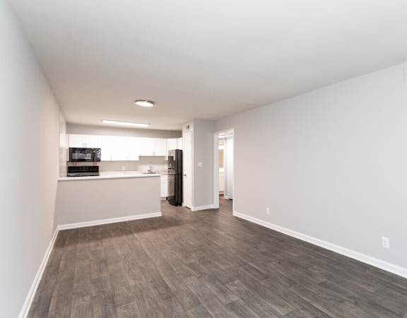 the living room and kitchen of an apartment with white walls and wood floors