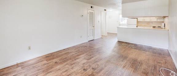the living room and kitchen of an apartment with wood flooring and white walls