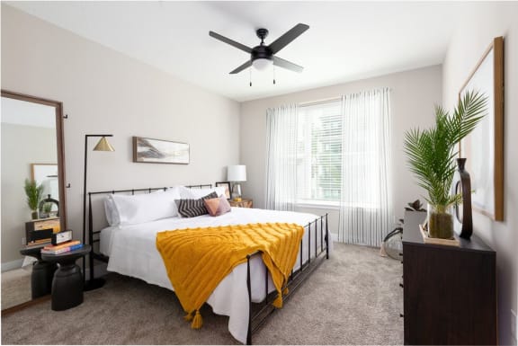 A bedroom with a bed, a ceiling fan, and a window with curtains at 19 South Apartments in Kissimmee, FL