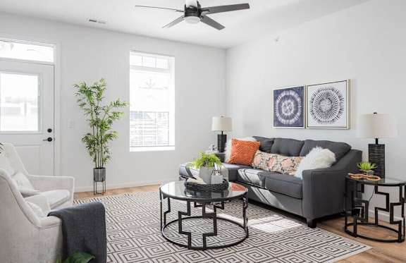 A living room with a grey couch, a black and white patterned rug, and a ceiling fan.